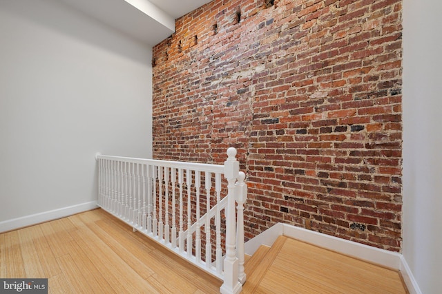 hallway with brick wall, wood finished floors, an upstairs landing, and baseboards