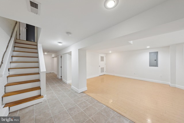 finished below grade area featuring visible vents, light wood-style floors, electric panel, baseboards, and stairs