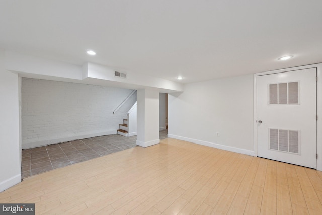 finished below grade area with stairs, visible vents, brick wall, and wood finished floors