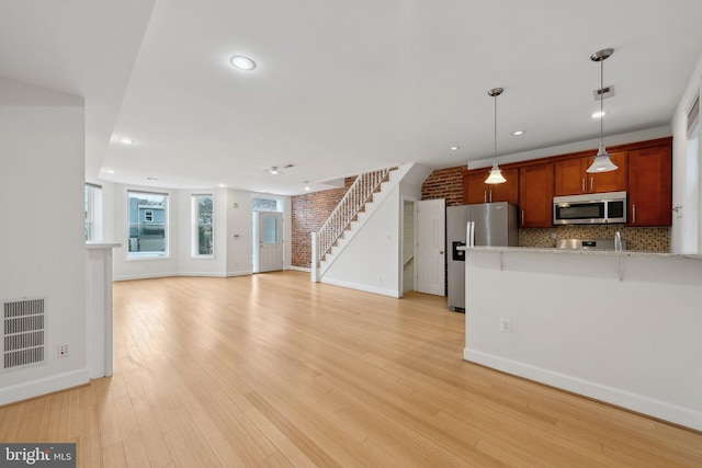 unfurnished living room featuring light wood-type flooring, stairway, brick wall, and visible vents