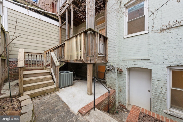 view of exterior entry featuring cooling unit, brick siding, and a patio