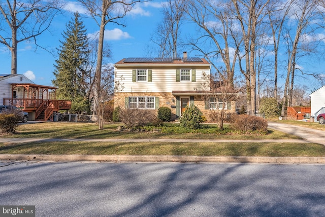 view of front facade featuring a front yard, roof mounted solar panels, brick siding, and a chimney