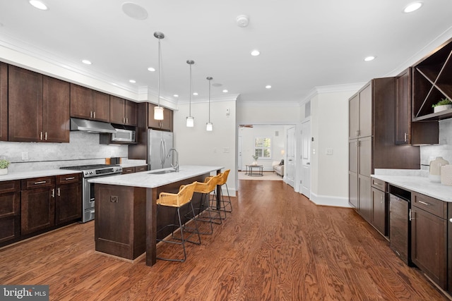 kitchen featuring a center island with sink, a kitchen bar, stainless steel appliances, hanging light fixtures, and dark brown cabinets