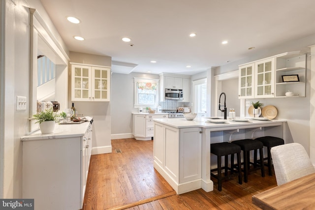 kitchen with glass insert cabinets, white cabinets, stainless steel microwave, and a breakfast bar area