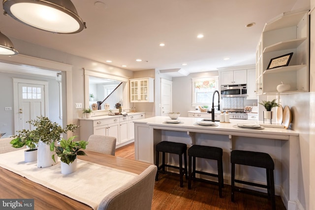 kitchen featuring light countertops, stainless steel microwave, glass insert cabinets, white cabinetry, and a kitchen bar