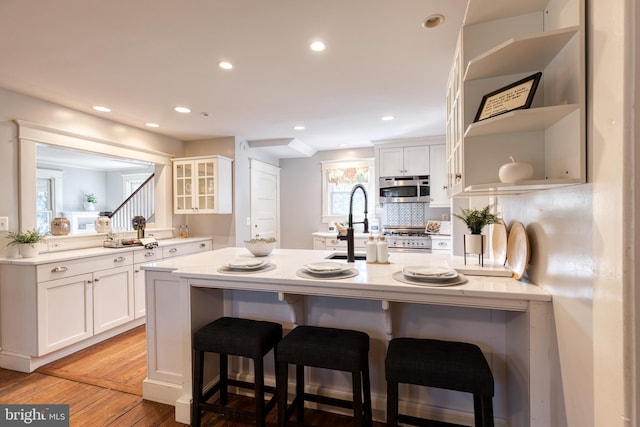 kitchen with open shelves, stainless steel microwave, white cabinets, and a kitchen breakfast bar