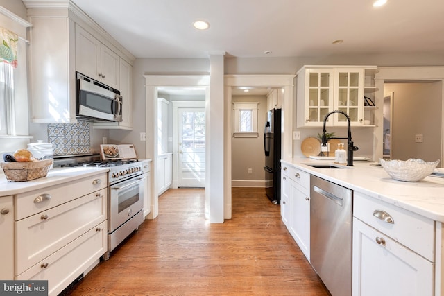 kitchen featuring light wood finished floors, stainless steel appliances, recessed lighting, glass insert cabinets, and a sink