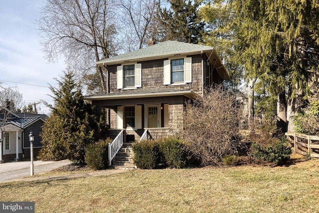 view of front of house with a shingled roof, a front yard, covered porch, and a chimney