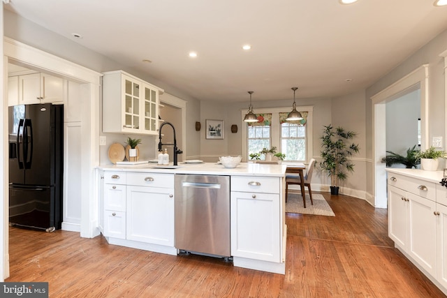 kitchen featuring a peninsula, stainless steel dishwasher, light countertops, and black fridge