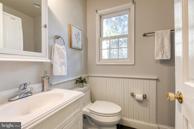 half bath with a wainscoted wall, vanity, and toilet