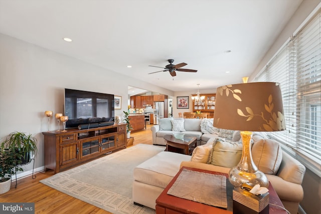 living area with recessed lighting, light wood-style flooring, baseboards, and ceiling fan with notable chandelier