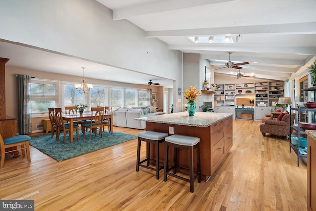 kitchen featuring lofted ceiling with beams, ceiling fan with notable chandelier, a kitchen island, open floor plan, and light wood finished floors