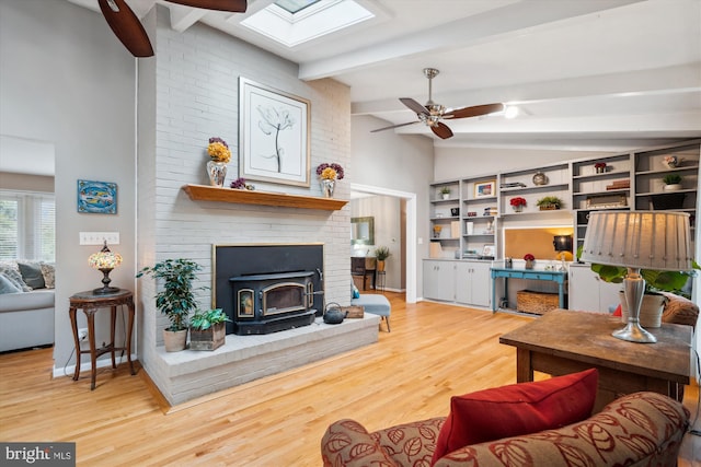 living area with a ceiling fan, a wood stove, wood finished floors, vaulted ceiling with skylight, and baseboards