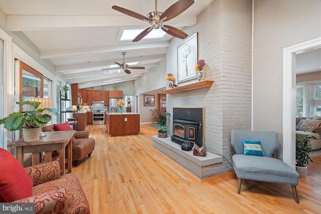 living room featuring a ceiling fan, light wood-type flooring, a wood stove, and vaulted ceiling with beams