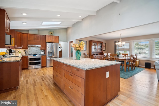 kitchen with vaulted ceiling with skylight, under cabinet range hood, stainless steel appliances, a kitchen island, and a sink