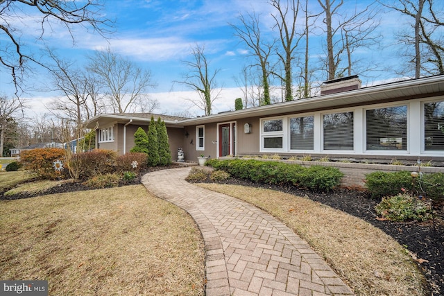 ranch-style home with a front yard, stucco siding, and a chimney