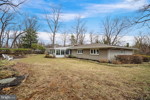 back of house with a sunroom, brick siding, a lawn, and a chimney