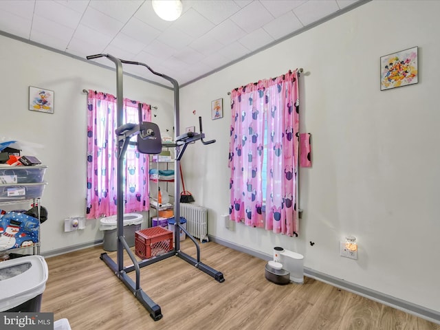 exercise room featuring light wood-style floors, baseboards, crown molding, and radiator heating unit