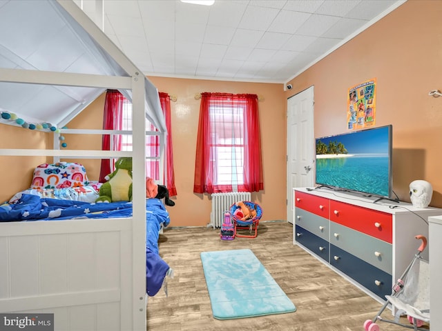 bedroom featuring lofted ceiling, radiator heating unit, and wood finished floors