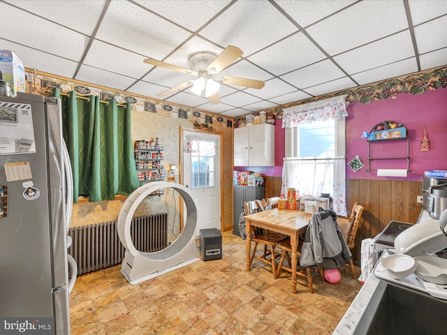 laundry room featuring a wainscoted wall, ceiling fan, wooden walls, and radiator heating unit