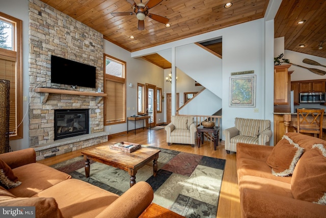 living area with light wood-style floors, ceiling fan, a stone fireplace, high vaulted ceiling, and wooden ceiling