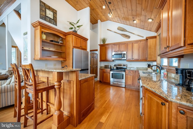 kitchen with brown cabinetry, wooden ceiling, appliances with stainless steel finishes, a breakfast bar, and light stone counters