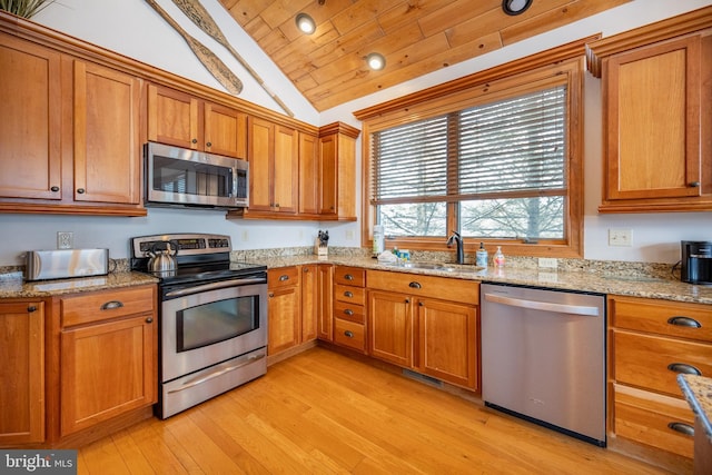 kitchen with stainless steel appliances, brown cabinets, a sink, and light stone counters