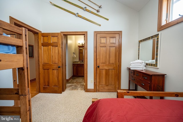 bedroom with ensuite bathroom, a high ceiling, baseboards, and light colored carpet