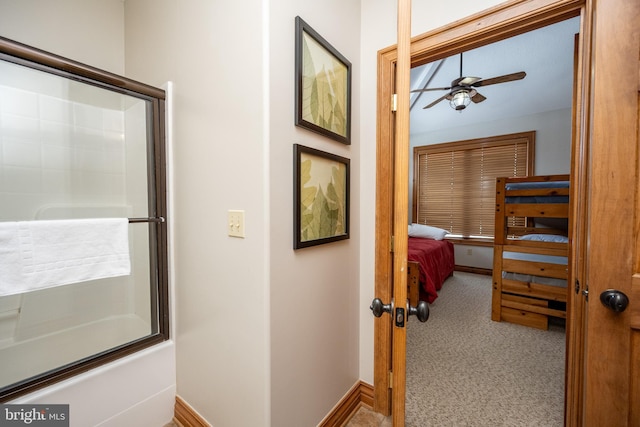 interior space featuring enclosed tub / shower combo, ensuite bath, a ceiling fan, and baseboards