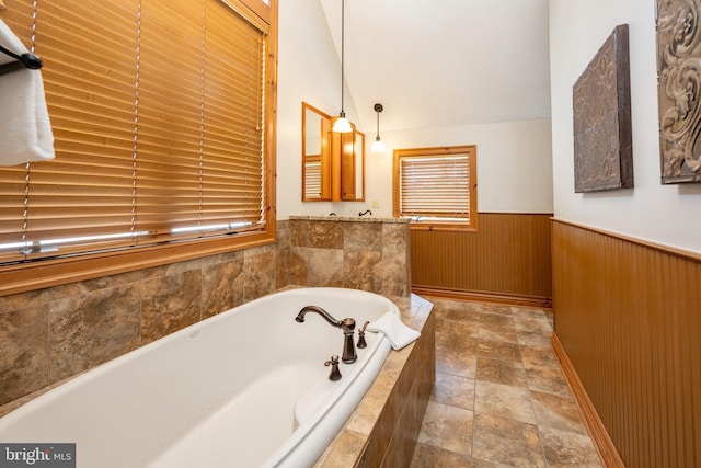 bathroom with lofted ceiling, a wainscoted wall, wooden walls, and a bath