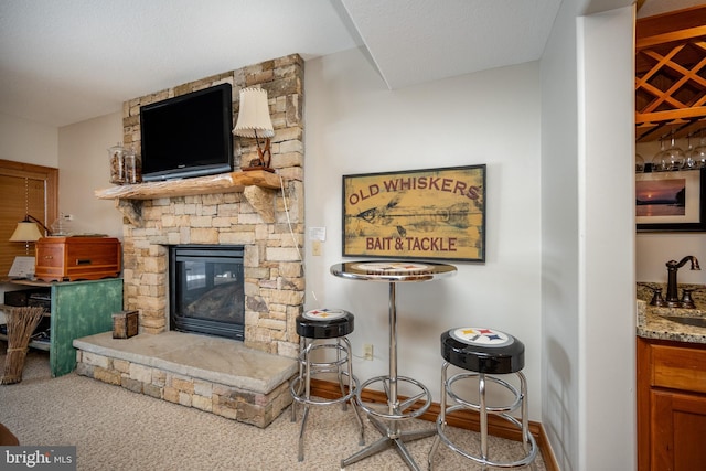 living room featuring indoor wet bar, a stone fireplace, and baseboards