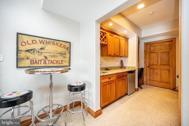 kitchen with baseboards, brown cabinetry, light colored carpet, light stone counters, and recessed lighting