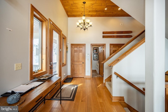 entrance foyer featuring light wood-style flooring, an inviting chandelier, wood ceiling, baseboards, and stairs