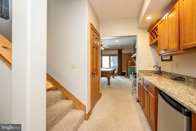 kitchen featuring dishwashing machine, recessed lighting, a sink, light stone countertops, and brown cabinetry