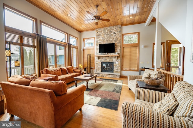 living area featuring light wood finished floors, a towering ceiling, wood ceiling, ceiling fan, and a fireplace