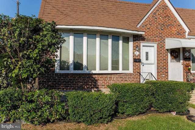 view of front of property featuring brick siding and roof with shingles