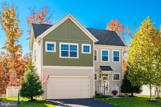 traditional-style home featuring aphalt driveway, a shingled roof, fence, a garage, and a front lawn