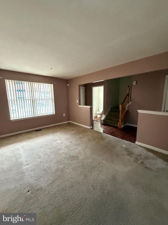 unfurnished living room featuring baseboards, stairs, and carpet