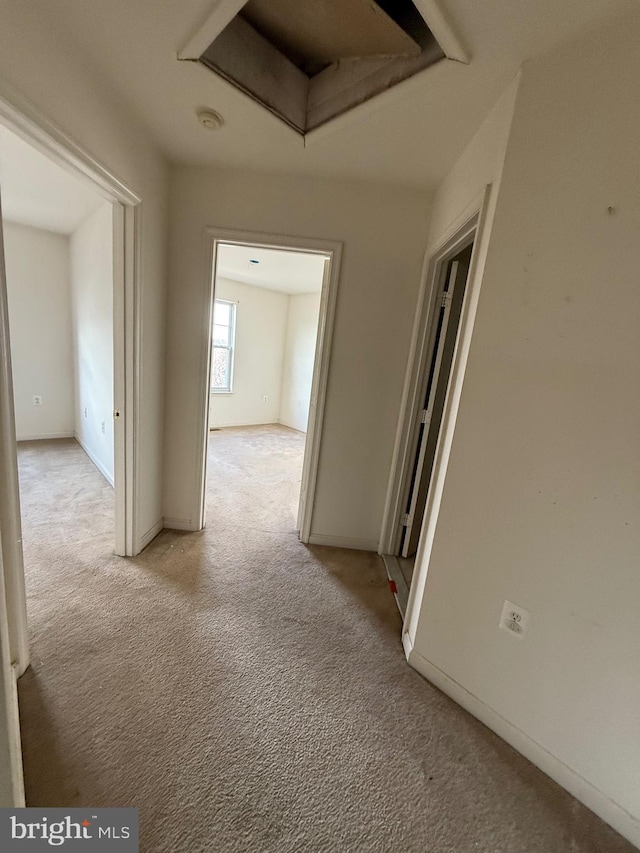 corridor featuring light colored carpet and baseboards