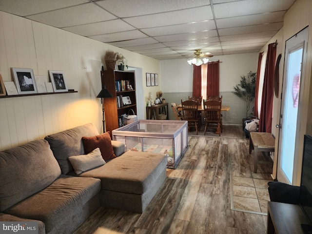 living area with a wainscoted wall, a drop ceiling, and wood finished floors