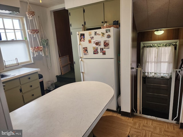 kitchen featuring pendant lighting, light countertops, freestanding refrigerator, and wooden walls