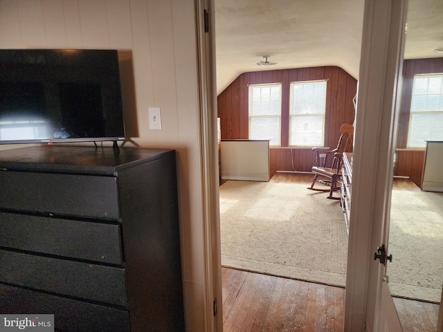 interior space with light wood-style flooring, wooden walls, and vaulted ceiling