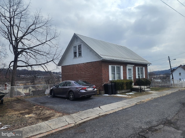 view of front of home with metal roof, brick siding, fence, and driveway