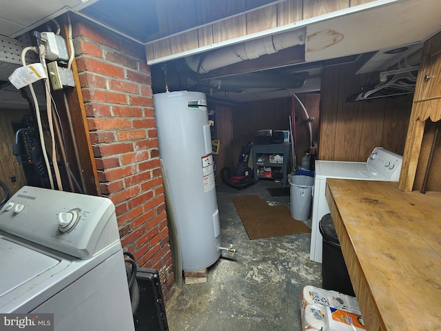 unfinished basement featuring wood walls, water heater, and washer and clothes dryer