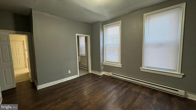 empty room with dark hardwood / wood-style flooring and a baseboard heating unit