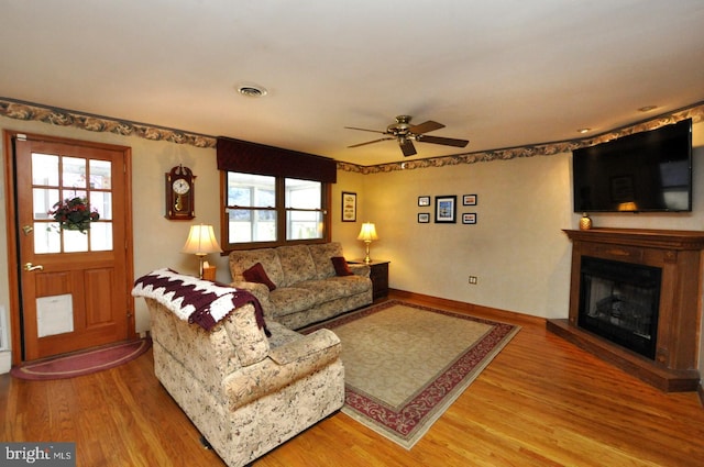 living area featuring a ceiling fan, wood finished floors, visible vents, and a fireplace with raised hearth