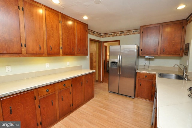 kitchen with light countertops, light wood-style floors, stainless steel fridge, and a sink