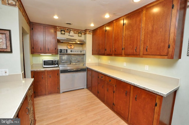 kitchen featuring stainless steel appliances, brown cabinets, light wood-style floors, and light countertops