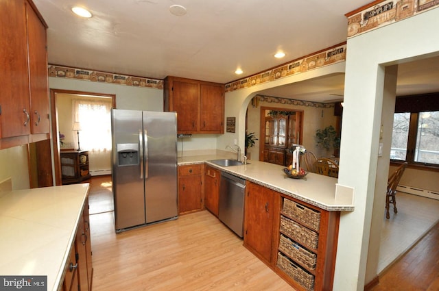 kitchen with light wood-style flooring, arched walkways, a sink, light countertops, and appliances with stainless steel finishes