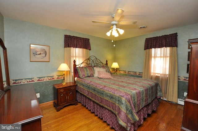 bedroom featuring a ceiling fan, wood finished floors, visible vents, and a baseboard radiator